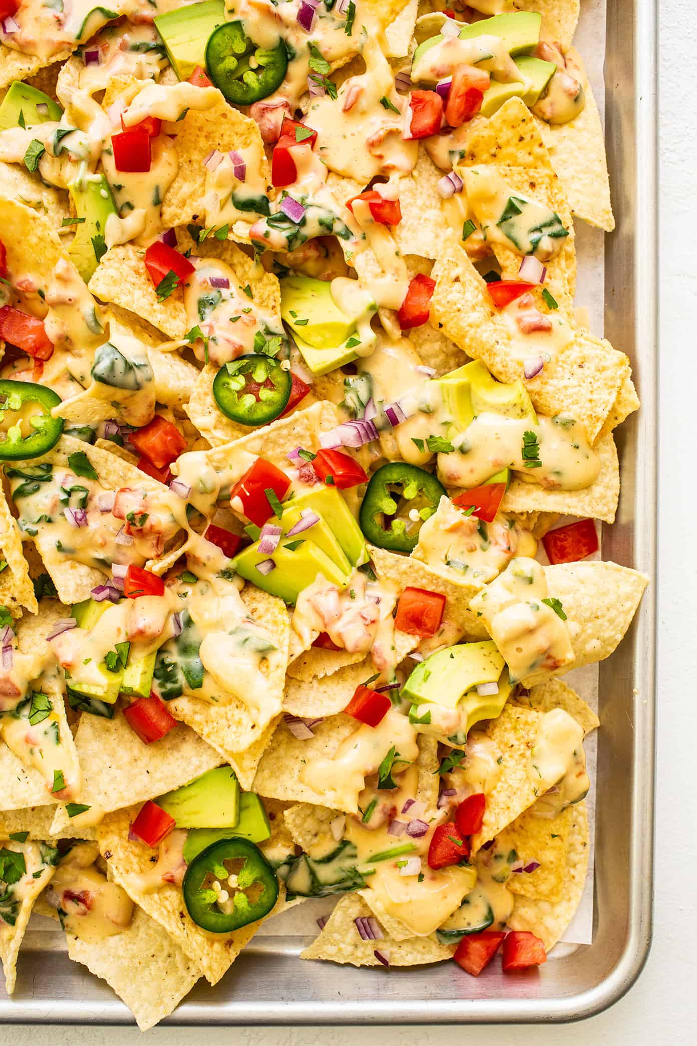 My go-to easy nachos recipe, made with my favorite Tex-Mex queso blanco dip, tortilla chips, avocado, tomato, red onion, jalapeรฑo and cilantro. Feel free to add meat, beans, salsa, or any other toppings that sound good too! | gimmesomeoven.com Favorite Easy Nachos