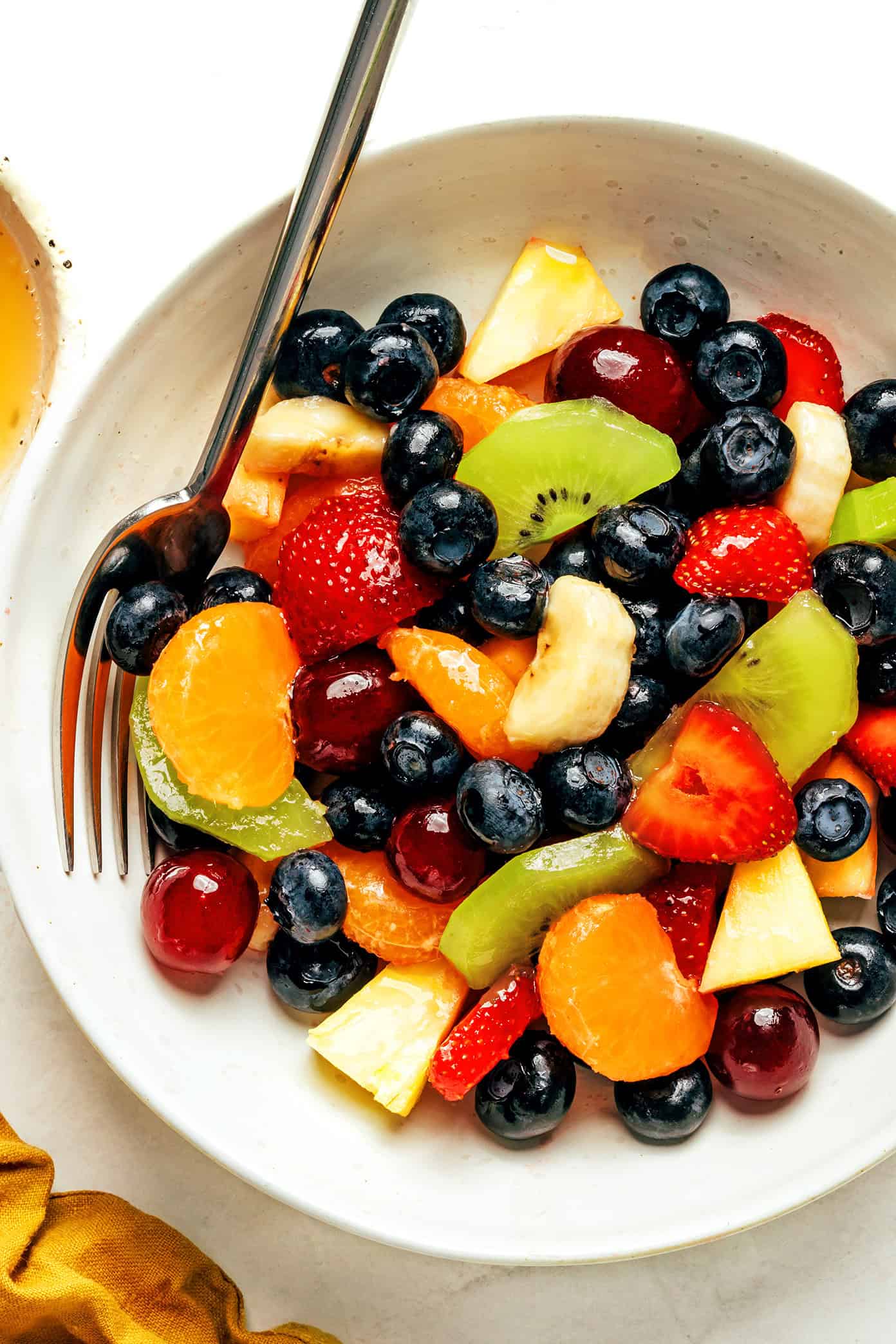 This easy fruit salad recipe features a rainbow mix of fresh fruit tossed in a zippy ginger-lime dressing. It's the perfect colorful side dish for picnics, grill nights or summer dinners! | gimmesomeoven.com bowl of fruit salad with fork