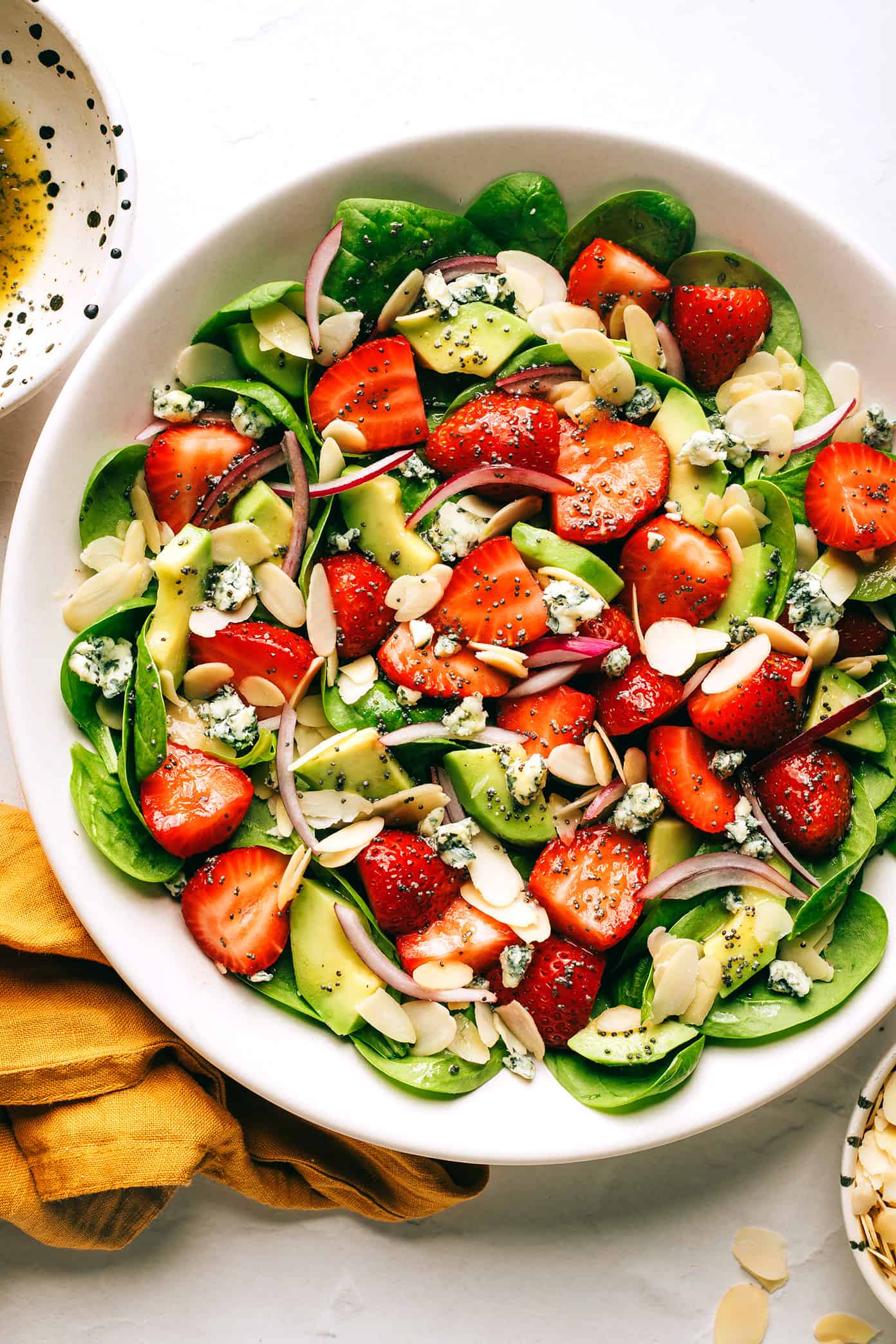 This fresh strawberry spinach salad recipe is tossed with creamy avocado, toasted almonds, sliced red onion, your choice of cheese (blue, feta, goat) and a lightly-sweetened honey poppyseed dressing. Feel free to add in some grilled chicken, shrimp or bacon if you'd like too! | gimmesomeoven.com Strawberry Avocado Spinach Salad with Poppyseed Dressing in Bowl
